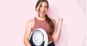 An excited woman in workout clothes holds a bathroom scale, pumping her fist in the air after her Semaglutide treatment in Scottsdale, AZ.