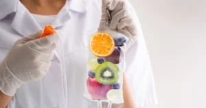 A person in a white lab coat and gloves holding an IV bag filled with fresh fruit, showcasing IV Therapy in Scottsdale, AZ.